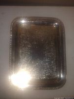 Rectangular silver plated copper serving platter with decorative engraved patterns and raised edge. Reflections and light glare visible on surface.