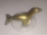 Photo of solid brass seal sculpture mounted on round white marble base, showing top and side views of the item.