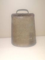 Front view of a vintage metal cow bell with handle, showing wear and patina.