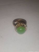 Photo showing round green gemstone set in gold-tone decorative bezel on ring band marked 925, size 8.5.