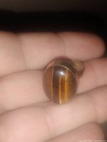 Close-up image of a vintage women's ring with an oval tiger eye stone held between fingers.