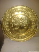 Photo of a brass decorative plate with embossed depiction of a Welsh woman by a fireplace, with ornate border.