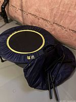 Mini trampoline with blue fabric cover and yellow trim, folded handle bars beside it, located on a basement floor with insulation wall in background.