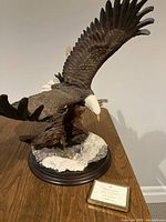 Large ceramic bald eagle figurine in flight with wide spread wings, perched on detailed base simulating natural elements and snow.