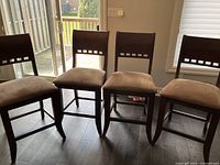 Four bar stools arranged side by side on dark hardwood floor showing overall set