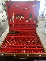 Entire open box showing full bronze flatware set arranged in red velvet-lined wooden case.