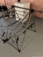 Metal folding drying rack shown partially from the side angle, displaying support bars and plastic connectors.