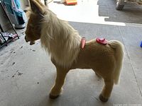 Side view of light brown mechanical horse with cream mane and tail, showing orange carrot and red brush on and next to its back