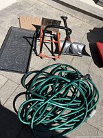 Wide view of the lot showing snow shovel, garden hose, two boot racks/trays, orange cart, and doormat