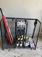 Full view of metal golf organizer holding shoes, umbrellas, and baskets with golf balls.