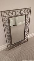 Full view of the heavy metal framed rectangular mirror resting against a wall on carpet. Mirror surface is clear and reflective.