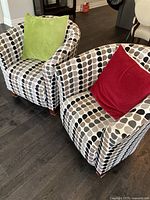 Two upholstered tub chairs with patterned fabric and green and red cushions placed on each chair on dark hardwood floor.