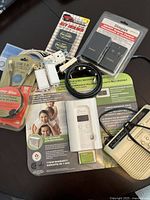 Top view of whole lot items including Kidde carbon monoxide detector in packaging, Dimplex fireplace remote in package, USB cable sealed, two light switches, key holder set, hide-a-key device.