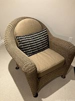 Front view of resin wicker patio chair showing taupe seat and back cushions with black-and-white geometric lumbar pillow