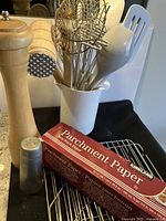 Photo showing four wire cooling racks, parchment paper box, large pepper grinder, salt grinder, assorted kitchen utensils in white holder, and vinegar bottle.