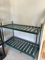 Full view of green metal shelf unit with two slatted shelves showing overall structure and condition