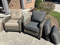 Two resin woven armchairs side by side on patio with one dressed in taupe cushions and one in slate grey cushions.