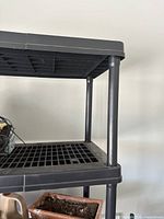 Close-up photo of the corner of the black plastic shelf showing the tubular support leg and grid-style surface.