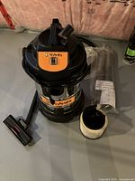 Overall view of the Kubota wet/dry shop vacuum with visible hose, filter, and nozzle attachment on concrete floor in basement.