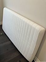 Single mattress topper standing upright showing quilted fabric cover.