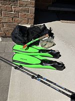 Photo showing Komperdell walking sticks, green AvantiHP flippers, snorkel, mask case, and mesh bag on pavement near brick wall