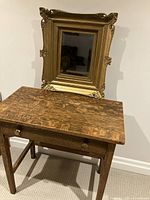Photo showing the antique table with mission style legs and single drawer beneath an ornate gold painted mirror.