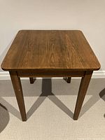 Front view of a square wooden occasional table showing the wood grain and straight tapered legs.