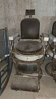 Front view of antique Koken barber chair showing padded seat, backrest and black finish.