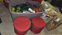 Wide shot showing plastic bin filled with multi-themed string lights and nearby red storage cases and baskets with other holiday items.