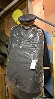 Olive green military dress uniform in plastic covering with gold buttons and sleeve insignia, hanging on rack.