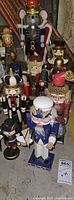 Full view of ten assorted nutcracker figurines standing upright. Includes a large mouse nutcracker, sailor, Santa, and multiple soldier-style nutcrackers with noted wear and dust.