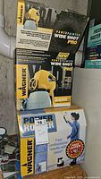 Photo of stacked original boxed Wagner PowerPainter Wide Shot Pro paint sprayer and Power Roller, showing brand and product details.