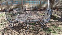 Overview photo of round metal mesh patio table and four matching metal chairs arranged outdoors with visible rust and weathering.