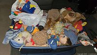 Plastic bin filled with various vintage plush toys, including dolls and stuffed animals in different colors and sizes.