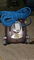 Top view of the robotic pool cleaner with coiled blue power cord on top, showing Kleen Machine logo and unit details.