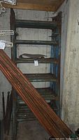 Overall view of stacked blue metal scaffolding frames with orange pipes leaning against them in a basement storage area