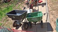 Two seed spreaders outdoors on a paved surface, one green Scotts SpeedyGreen 1000 model and one black PF 85 Poly model.