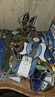 Photo showing assorted stained glass suncatchers piled together featuring a star-like tulip flower design and a blue angel figure