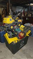 Wide view showing multiple Tonka and Nylint pressed steel trucks stacked in a large bin in a basement area.