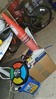 Photo showing large Crayola crayon plastic bank and other items in storage area with bicycle in background