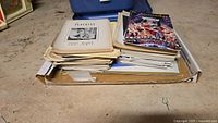 Stack of vintage playbills and programs in a shallow cardboard box, showing worn and aged paper with some yellowing.