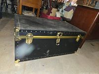 Black vintage steamer trunk exterior showing brass-tone latches and corner protectors.