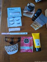 Overview of all beauty items on wooden surface: perfume, lash kit, hair clips, bath product, conditioning sachet, etc.