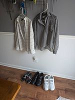 Two blouses hanging, two pairs of shoes and a pair of flip flops below them.