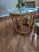 Side view showing end table with round glass top on natural rattan base in living room setting