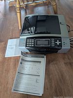 Photo of Brother multifunction printer on wooden floor with user manual and start guide in front