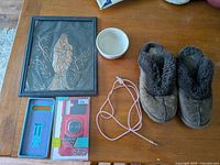 Overview of lot showing all items: copper picture frame, white ceramic bowl, brown Ugg slippers, two phone cases in packaging, and a charger cable on brown wood table