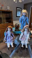 Three porcelain dolls displayed on stands, dressed in Victorian style clothing