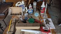 Photo showing assorted garage maintenance items including cans of oil, spray lubricant, glue, screws, springs, and a green garden hose.