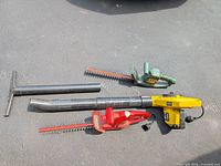 Two electric hedge trimmers and one yellow electric leaf blower laid out on pavement, showing overall condition and details of each tool.